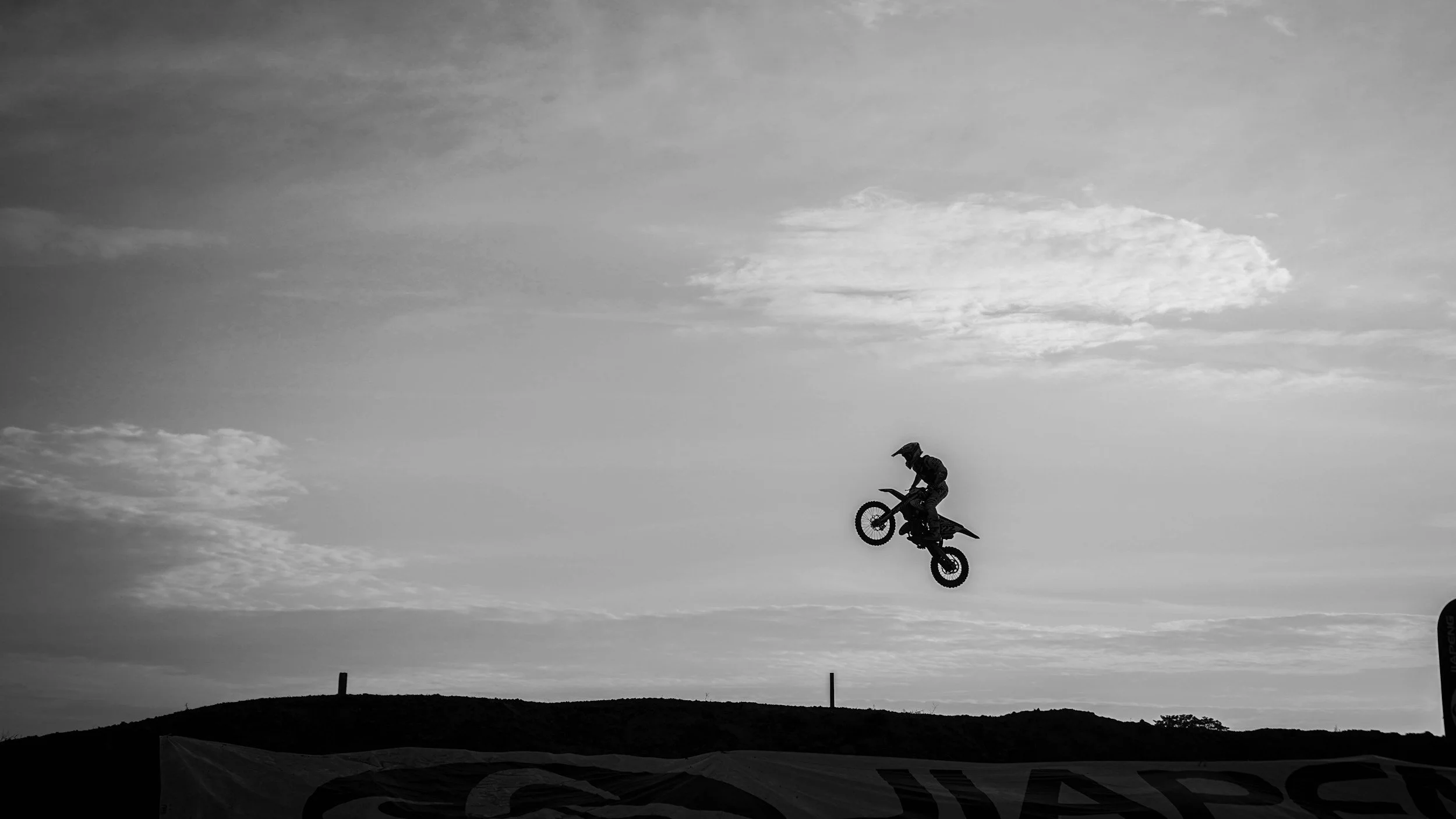 A person performing a jump on a mountain bike in silhouette against the sky with clouds.