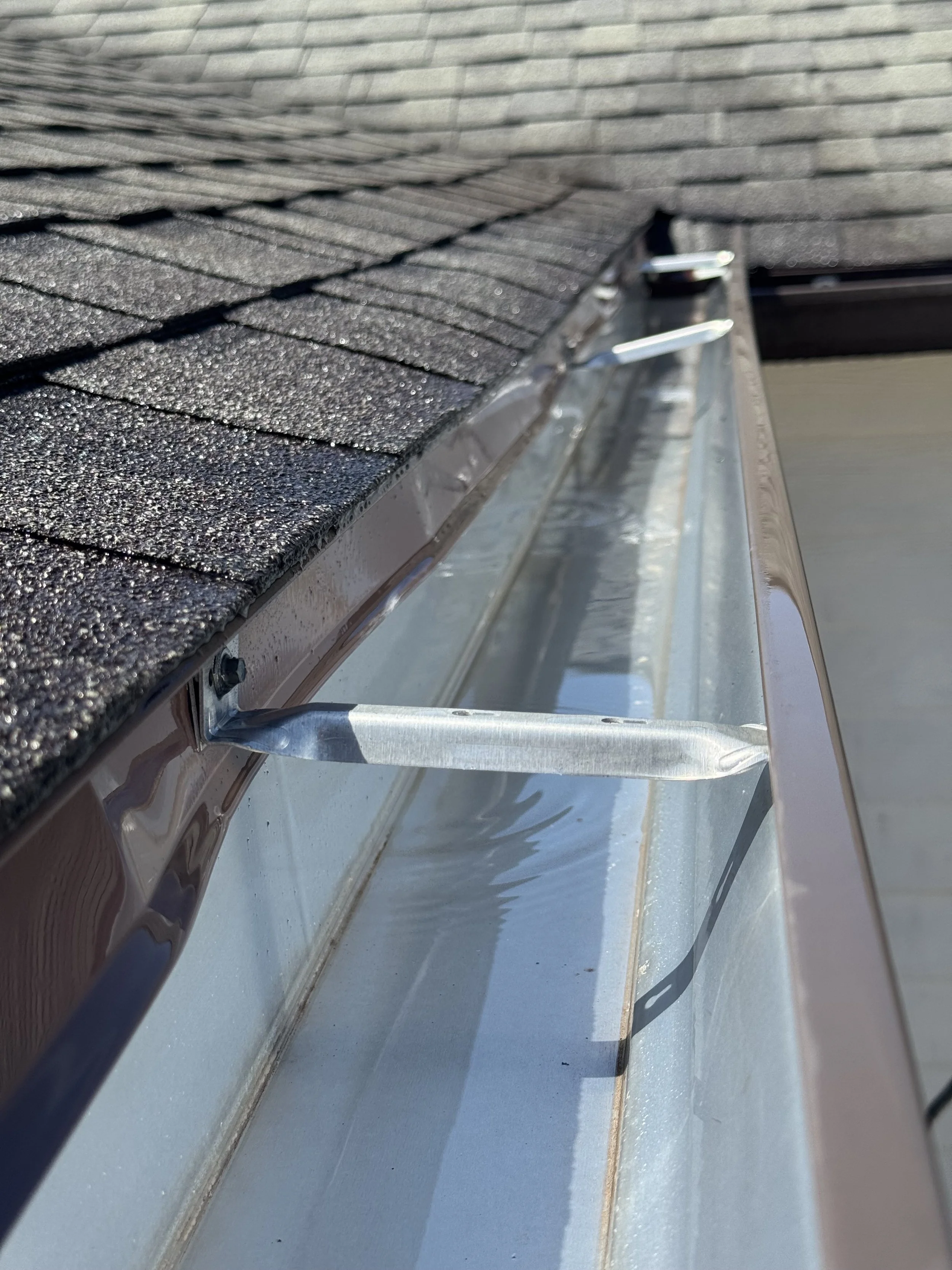 Close-up of a rooftop with black asphalt shingles and a metal gutter with a downspout.
