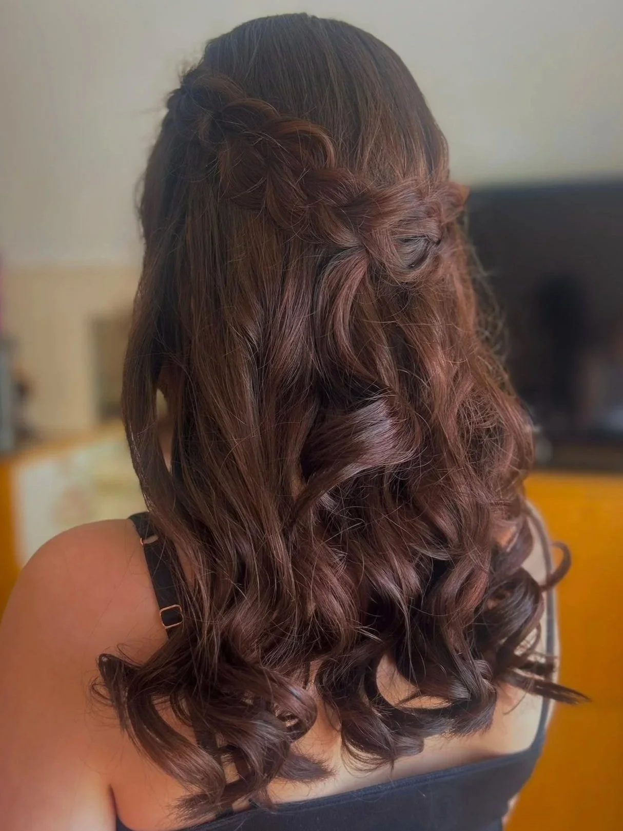 A woman with long, brown, curly hair styled in a half-up braid.