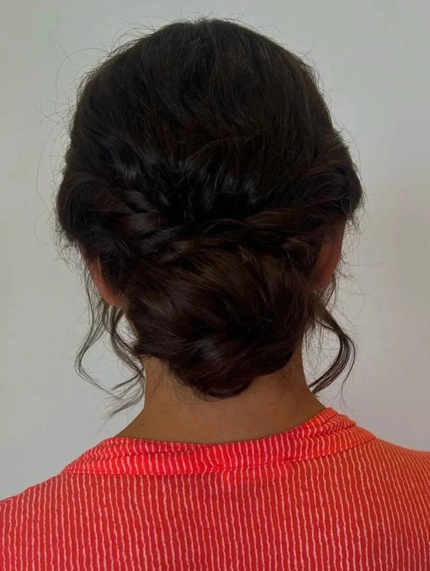 A woman with dark brown hair styled in an elegant updo viewed from the back, wearing a red and white striped shirt.