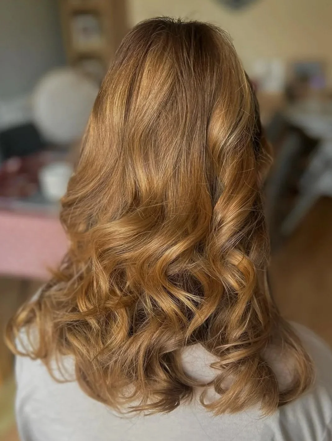 Back view of a woman with shoulder-length, wavy, caramel-colored hair.