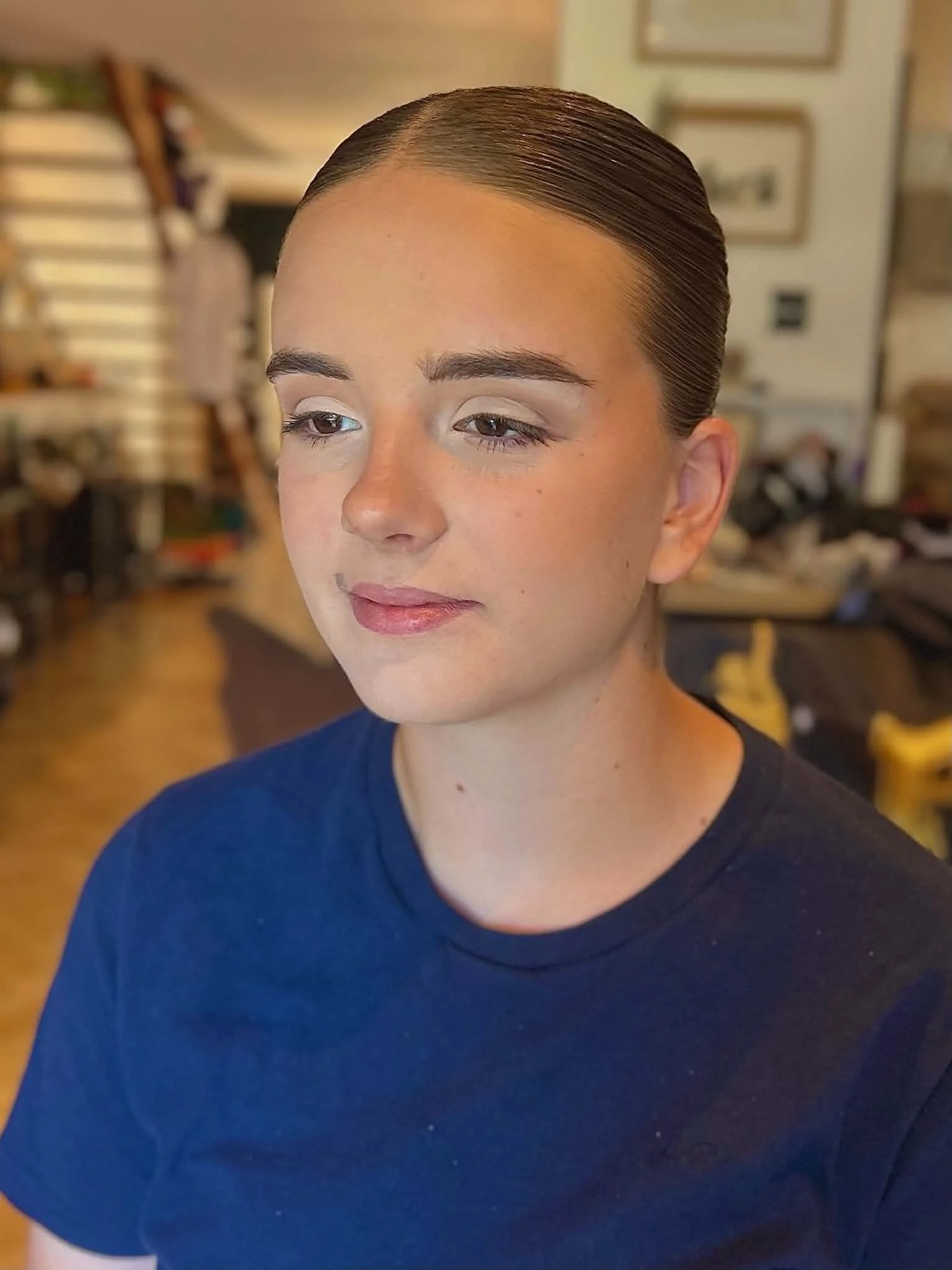 Close-up of a young woman with neatly styled slicked-back hair, with soft glam makeup.