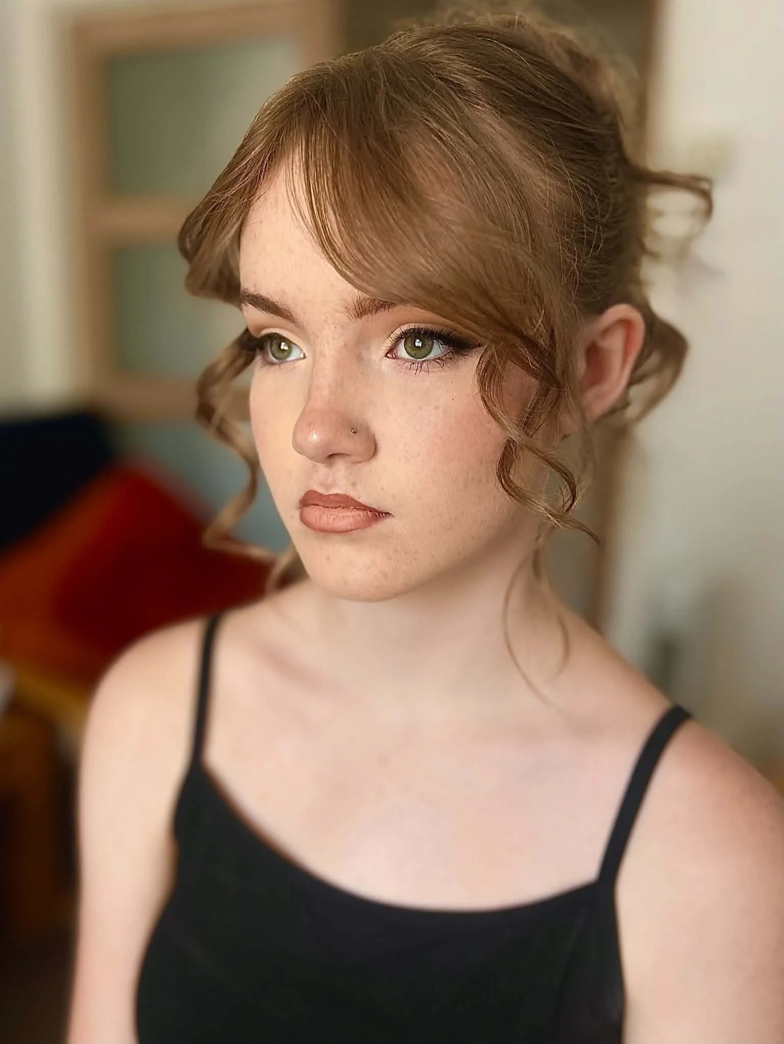 Close-up of a woman with reddish-brown hair styled in loose curls, with softy glam makeup with soft cat eye eyeliner.
