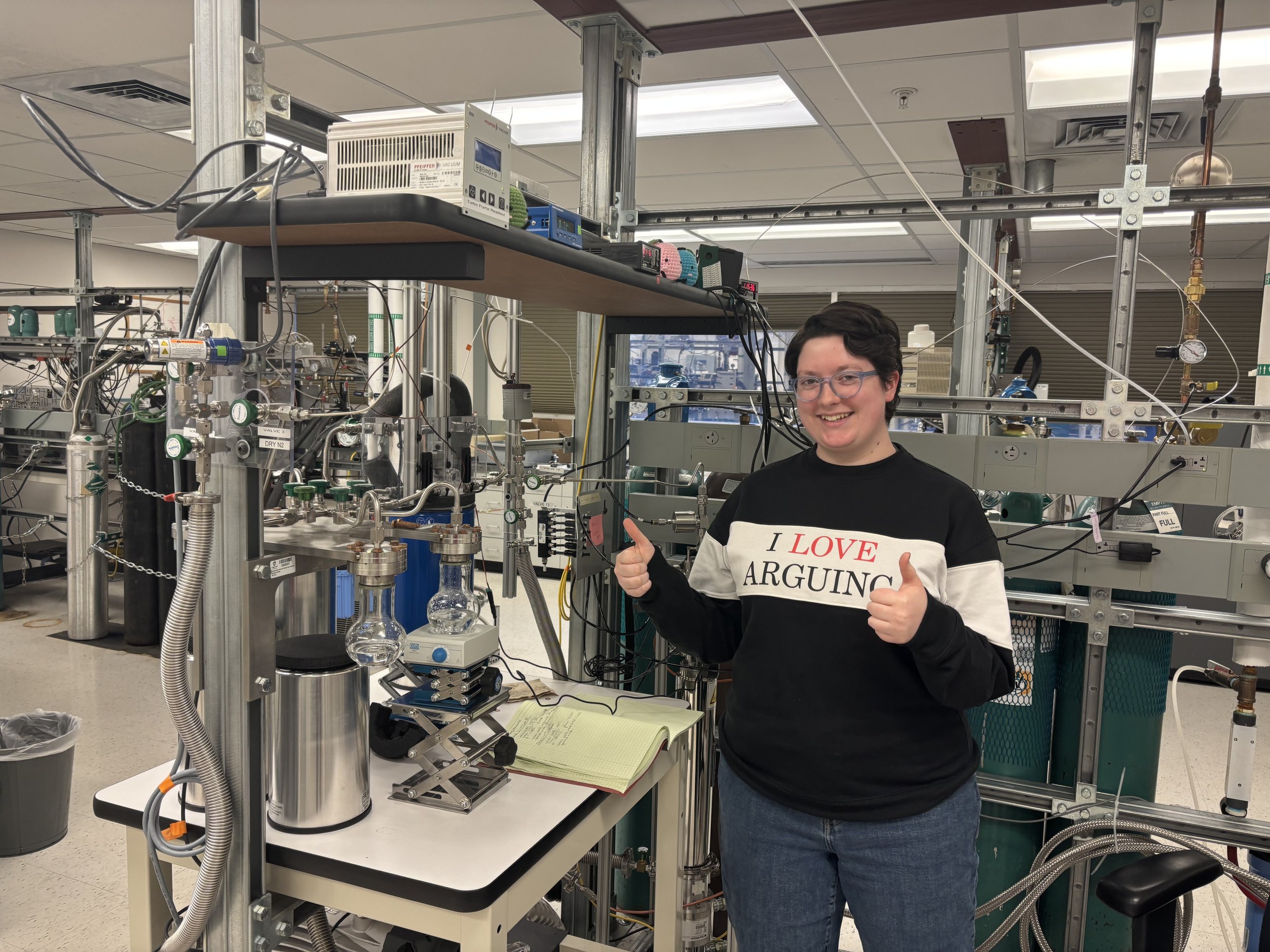 A Ph.D. student standing by a complex mechanism designed to extract noble gases.