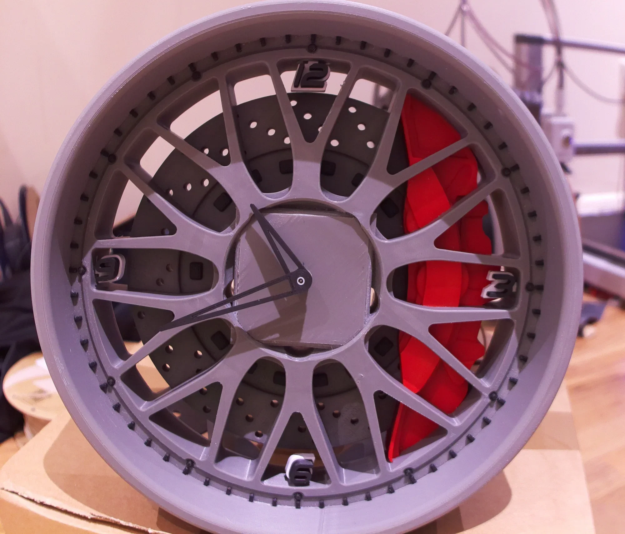 A complex mechanical clock with a gray plastic frame, visible gears, red components, and black hands showing the time on the clock face.