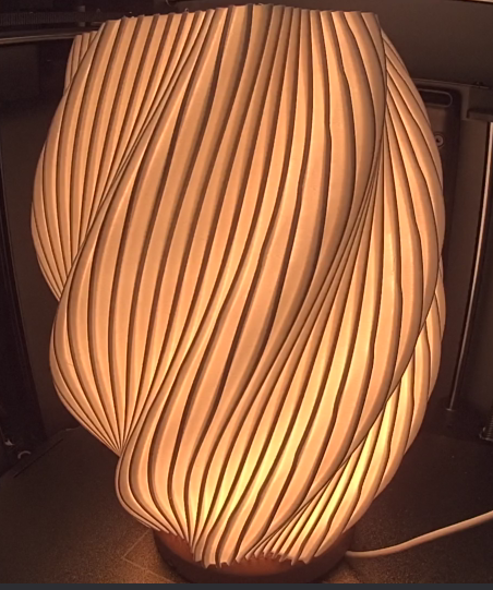 A decorative table lamp with a wavy, wooden slat design emitting a warm glow.
