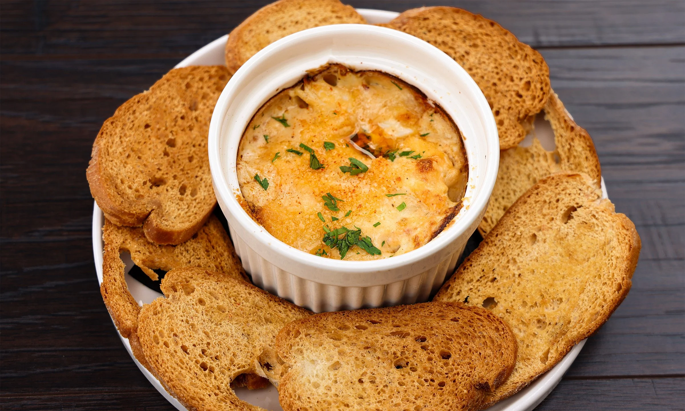 A white bowl of French onion soup garnished with herbs, surrounded by toasted bread slices on a white plate.