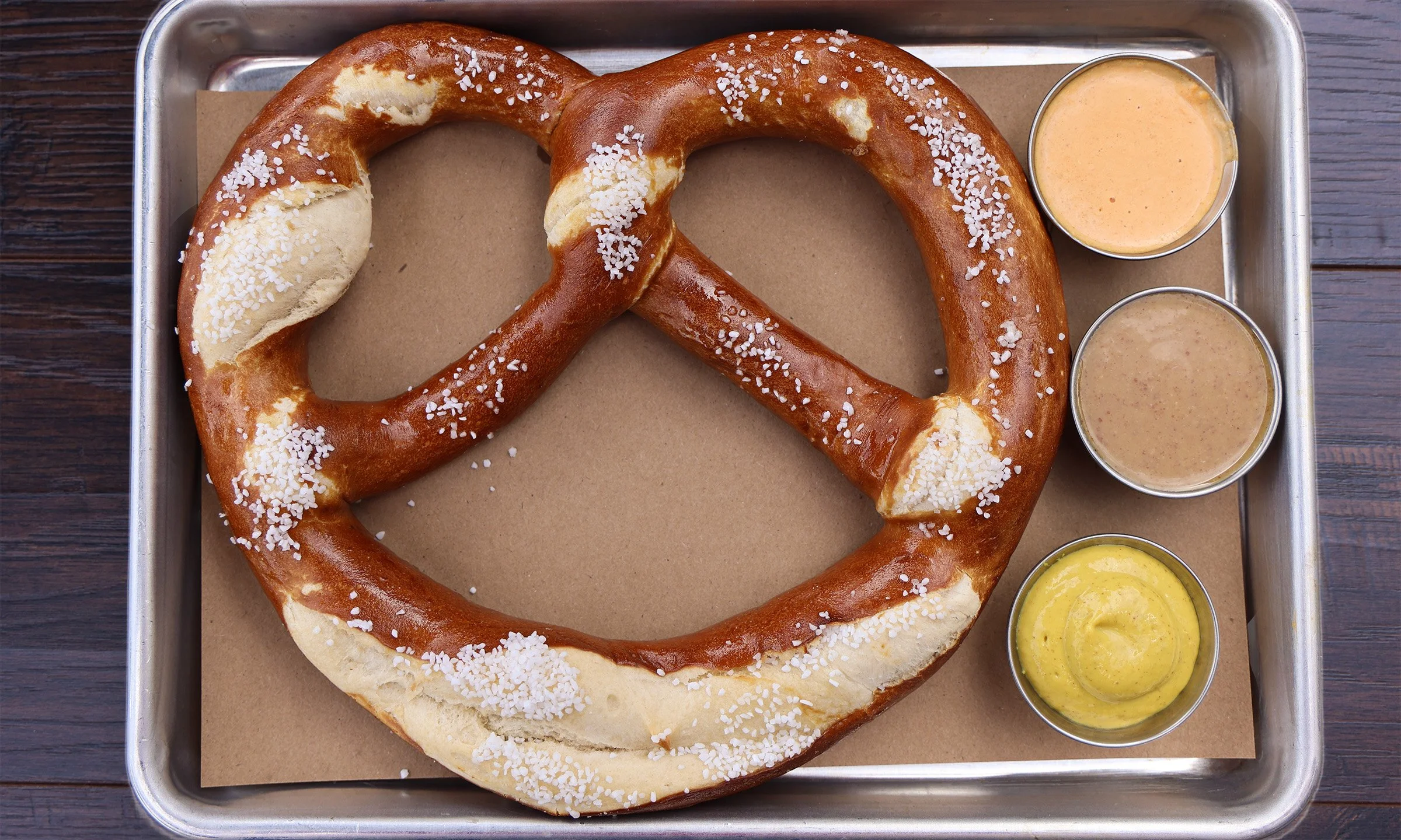 Large pretzel with coarse salt on a tray, served with three different dipping sauces.