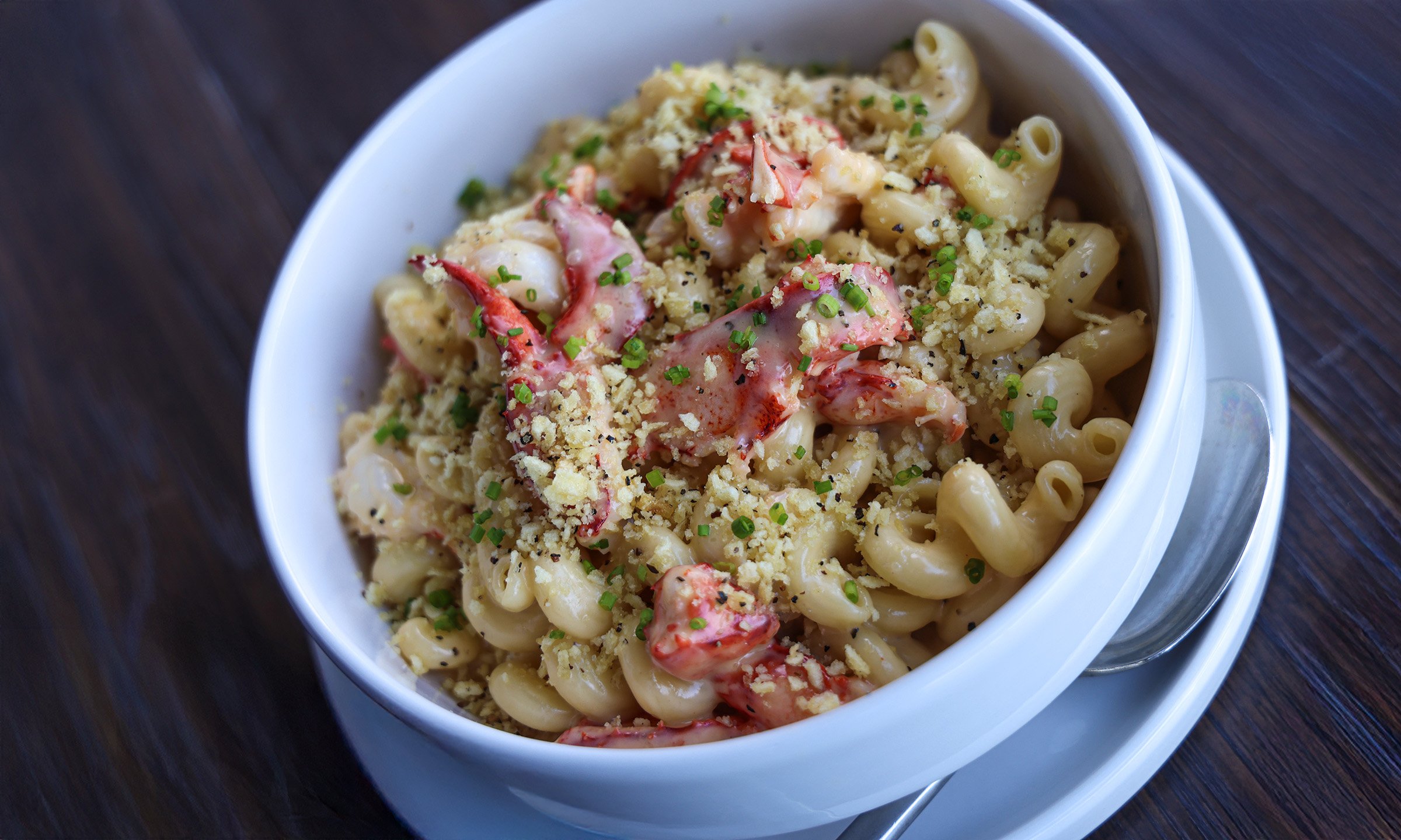 A bowl of creamy macaroni pasta with lobster pieces, topped with chopped herbs and bread crumbs.