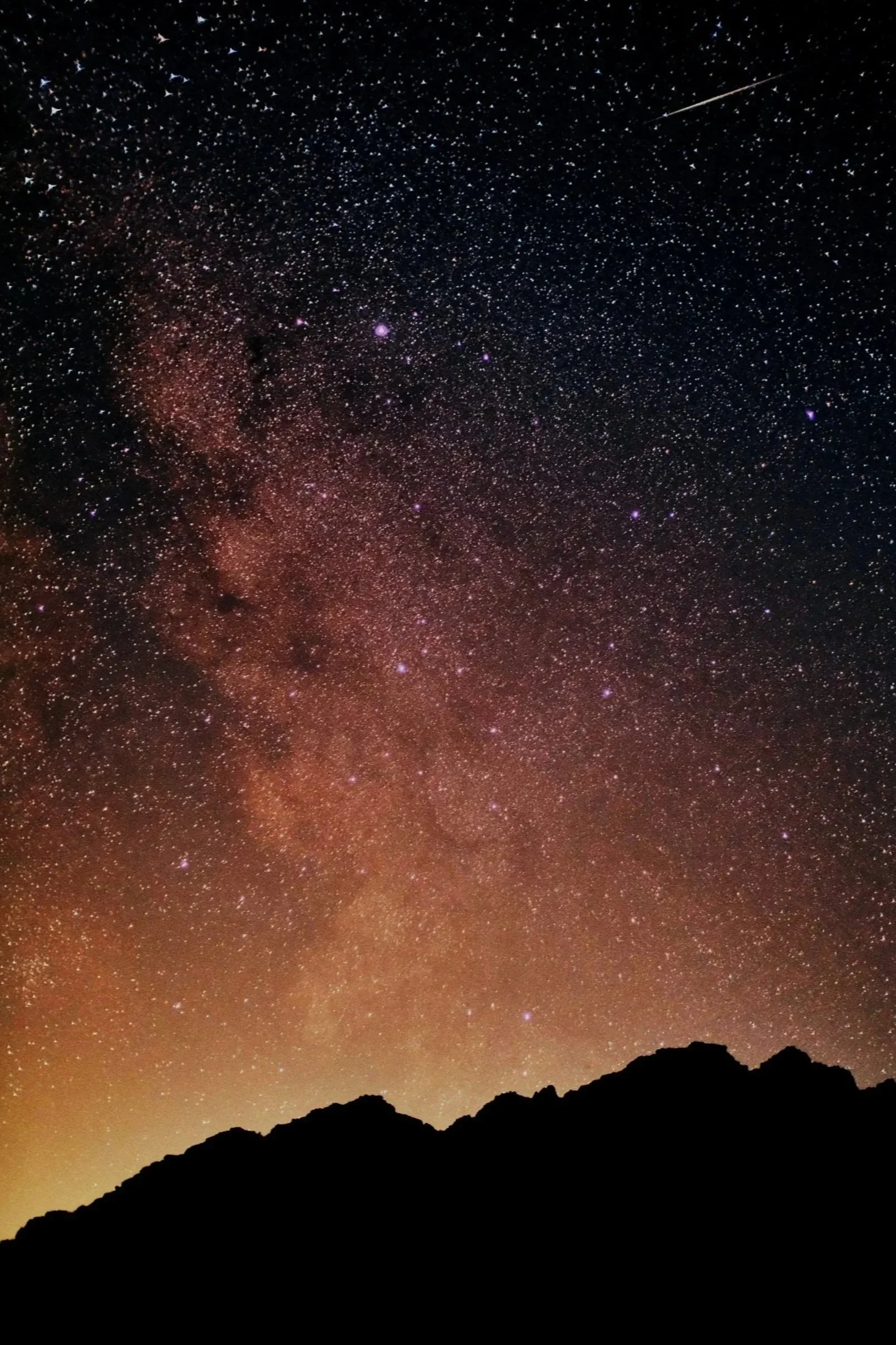 Star-filled night sky above dark mountain silhouettes.