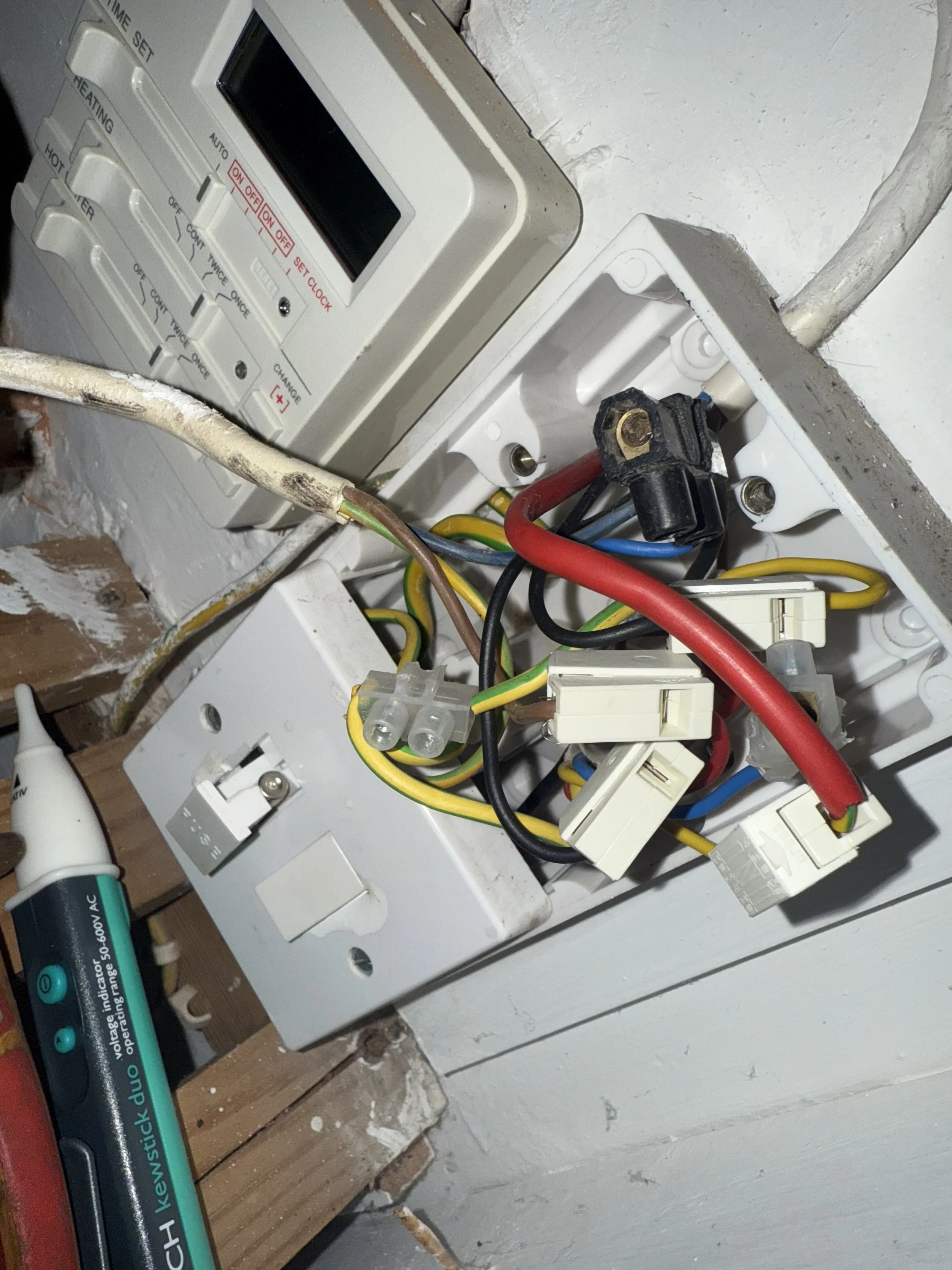 Open electrical box with tangled wires, circuit breaker, and a digital thermostat mounted on the wall.