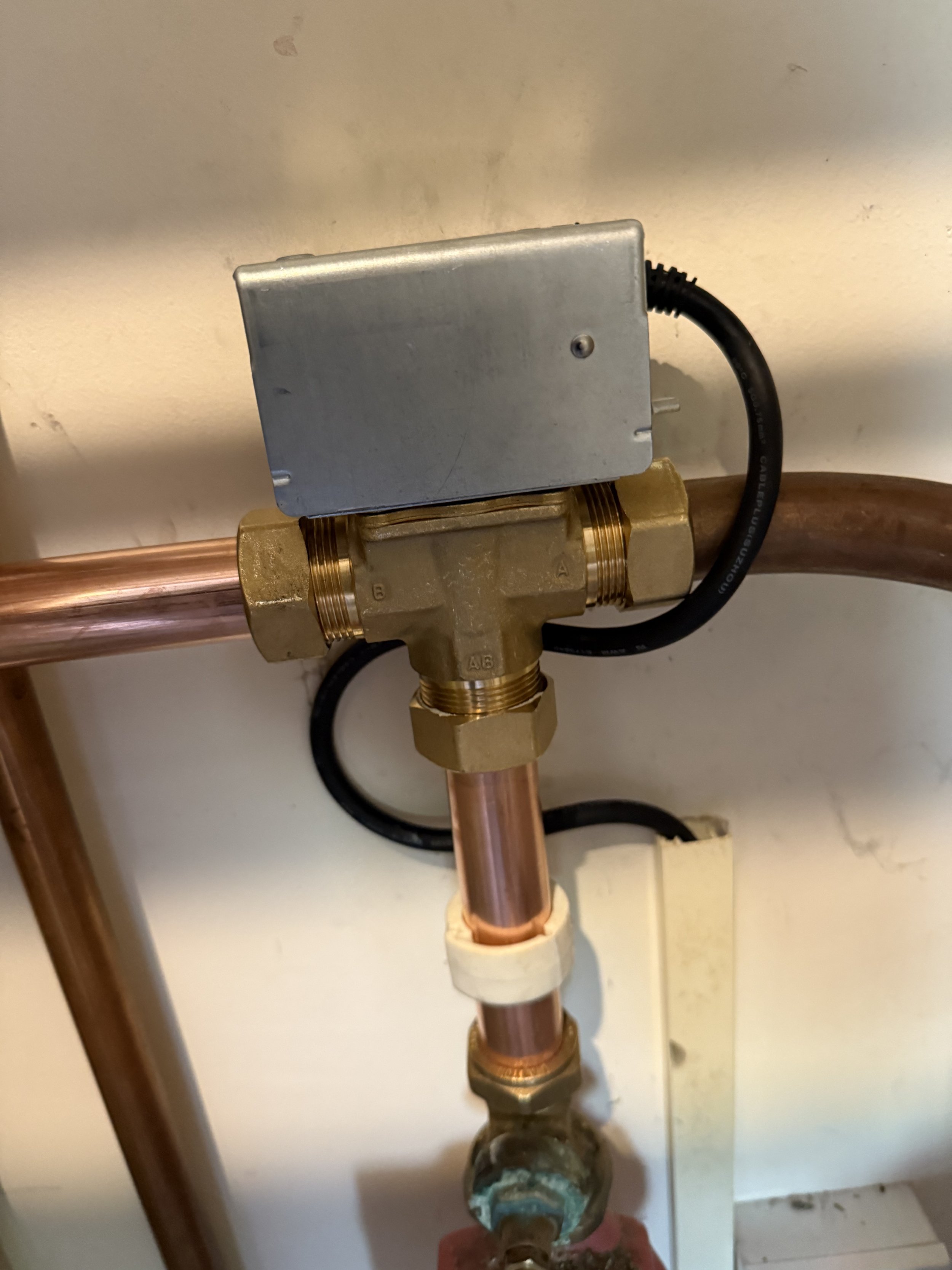 A plumbing control valve connected to copper pipes and an electrical box mounted on the wall.