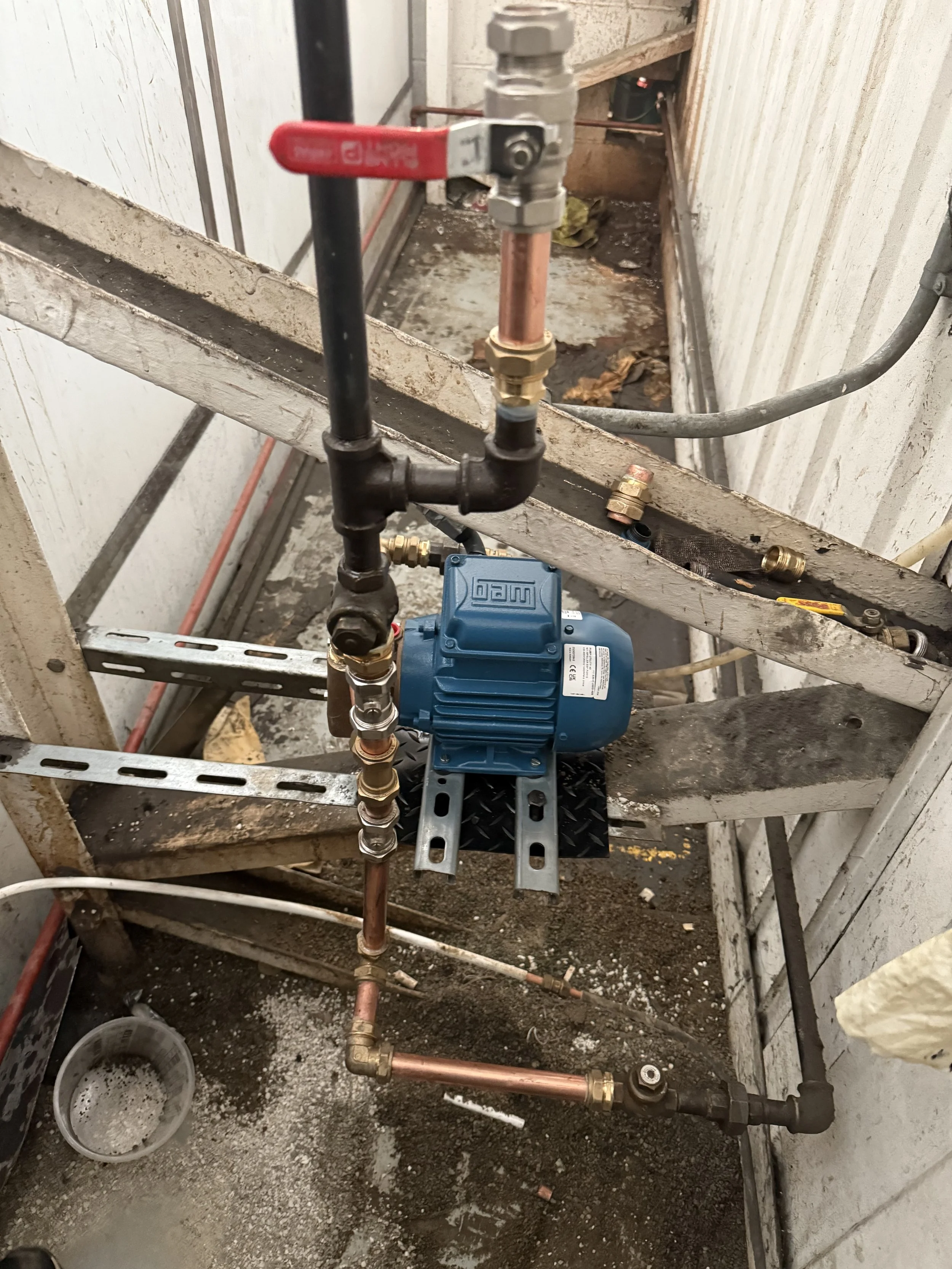 Close-up of plumbing system with a blue pump connected to copper and black pipes, on a construction frame in a building under construction.
