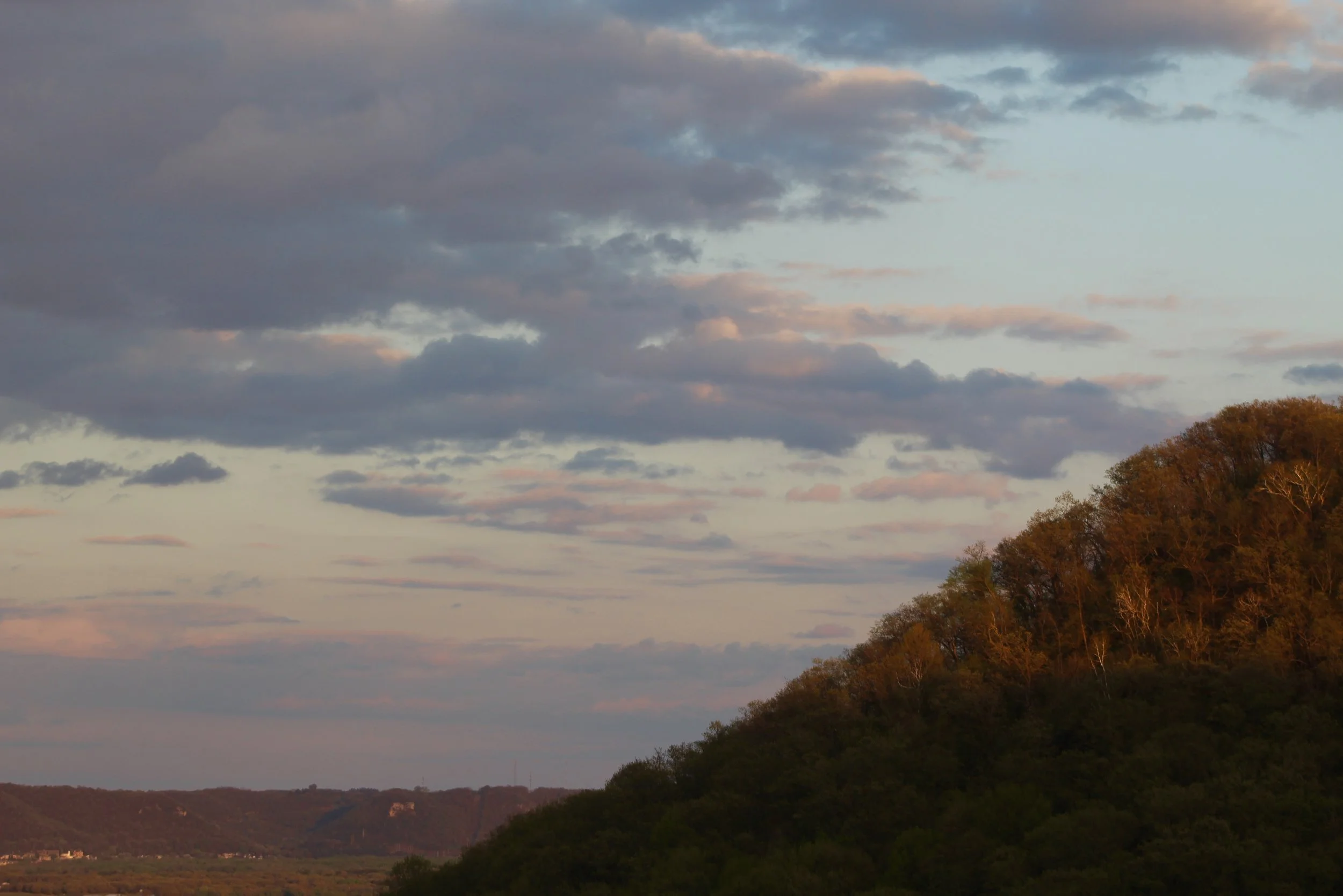 Scenic landscape at dusk with a sky filled with clouds and a hillside with trees in autumn colors.
