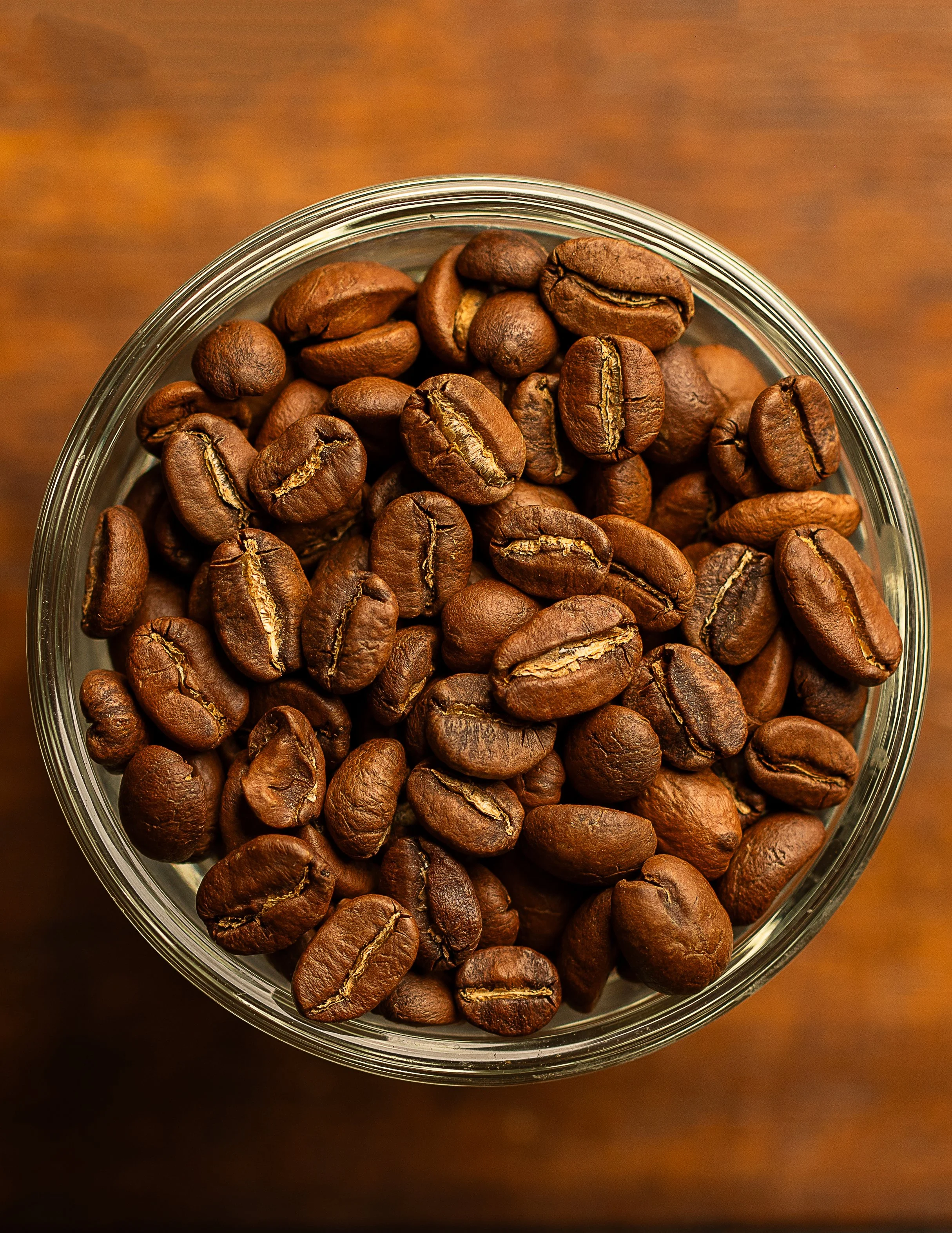 Close-up view of roasted coffee beans inside a glass jar, with a wooden surface background.