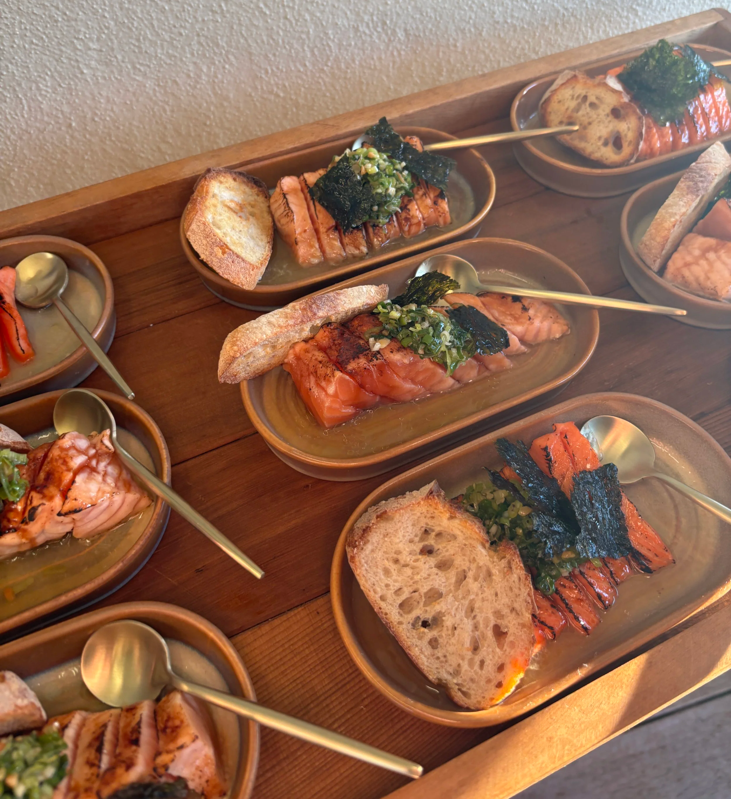 Assorted sushi rolls and grilled salmon with toast on a wooden serving tray.