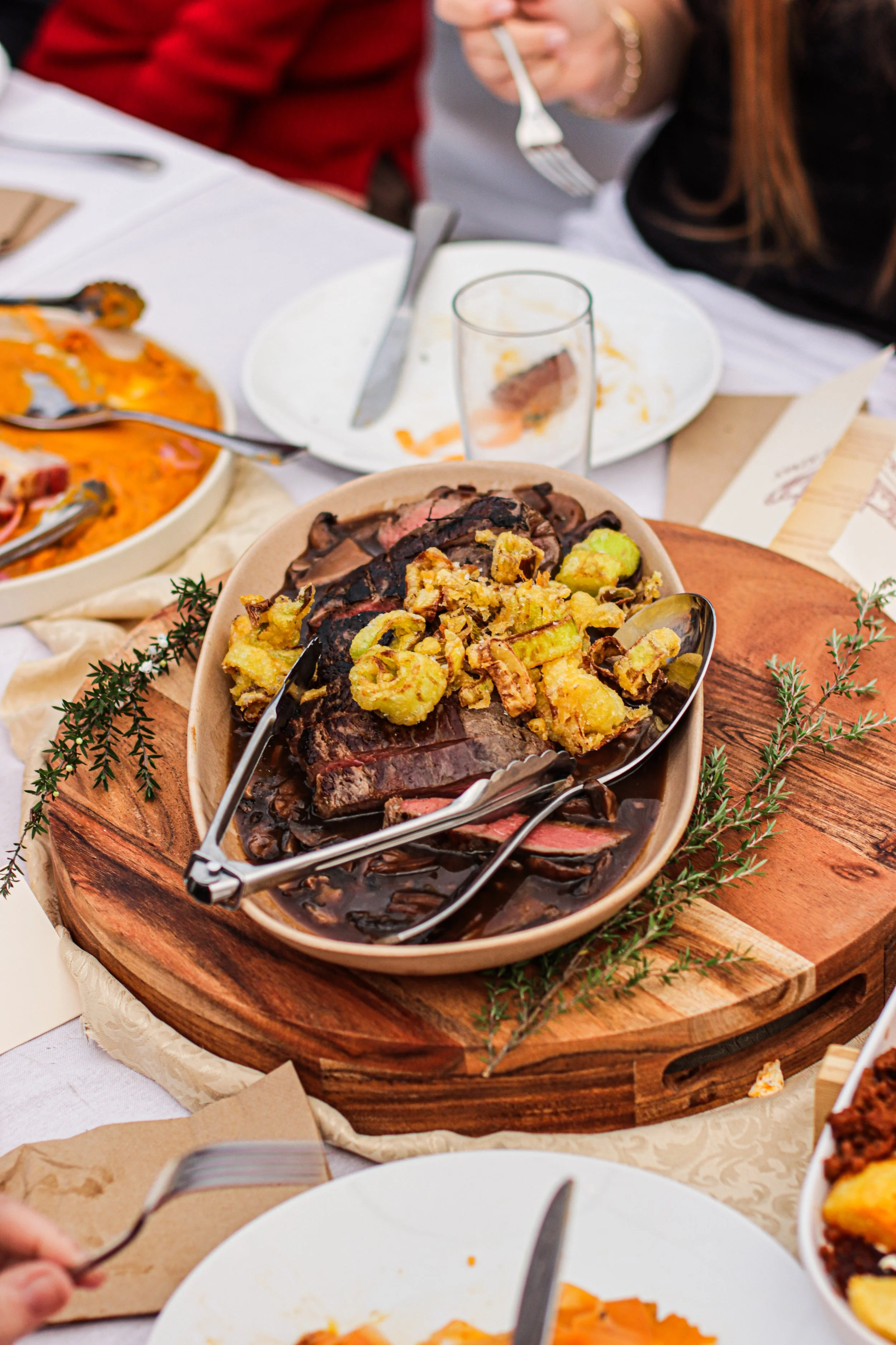 A table with a variety of dishes, including a roast beef with gravy, a vegetable casserole, and other side dishes, with people serving themselves at a family meal.
