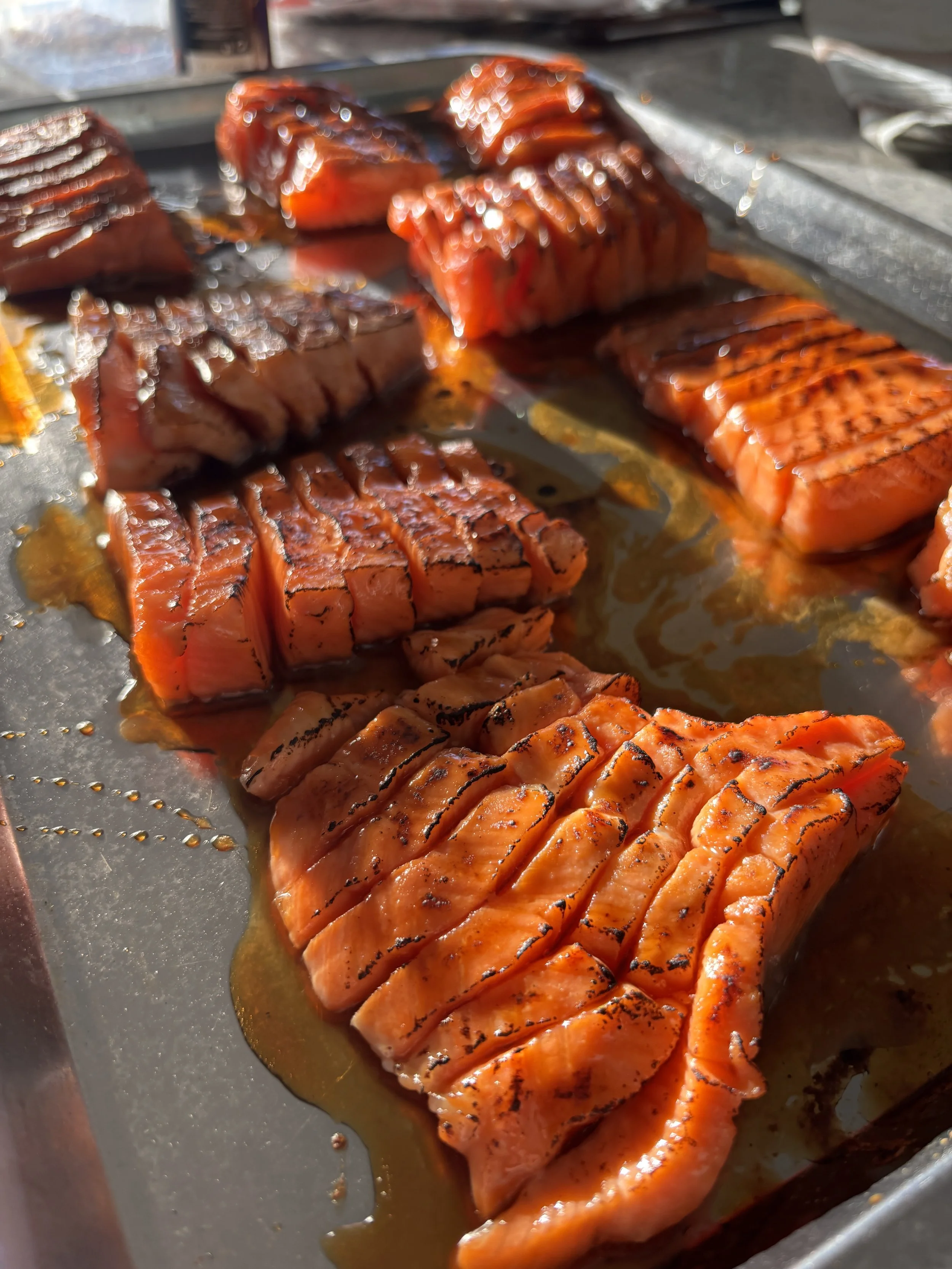 Grilled salmon fillet with grill marks on an oil-coated metal surface.