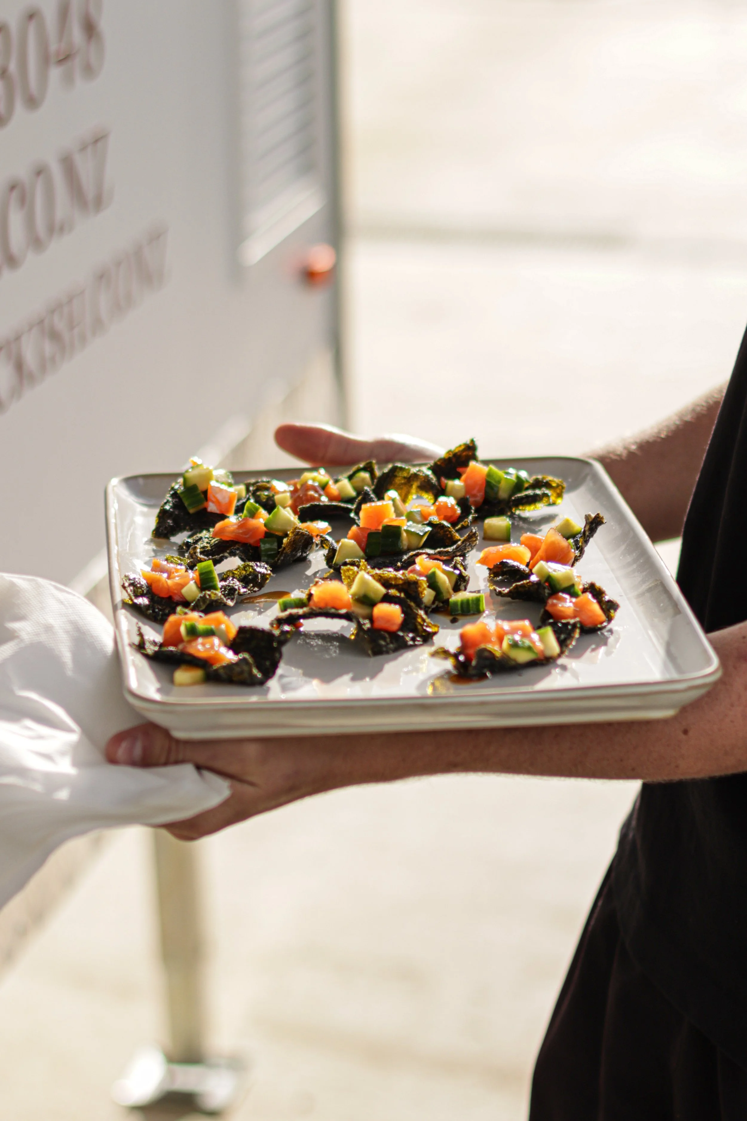 Person holding a plate of assorted topped crackers or flatbread appetizers, garnished with various colorful vegetables or toppings.