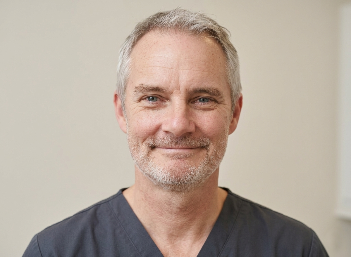 Our practitioner, Alan Dobson, wearing medical scrubs, smiling gently in a medical setting.