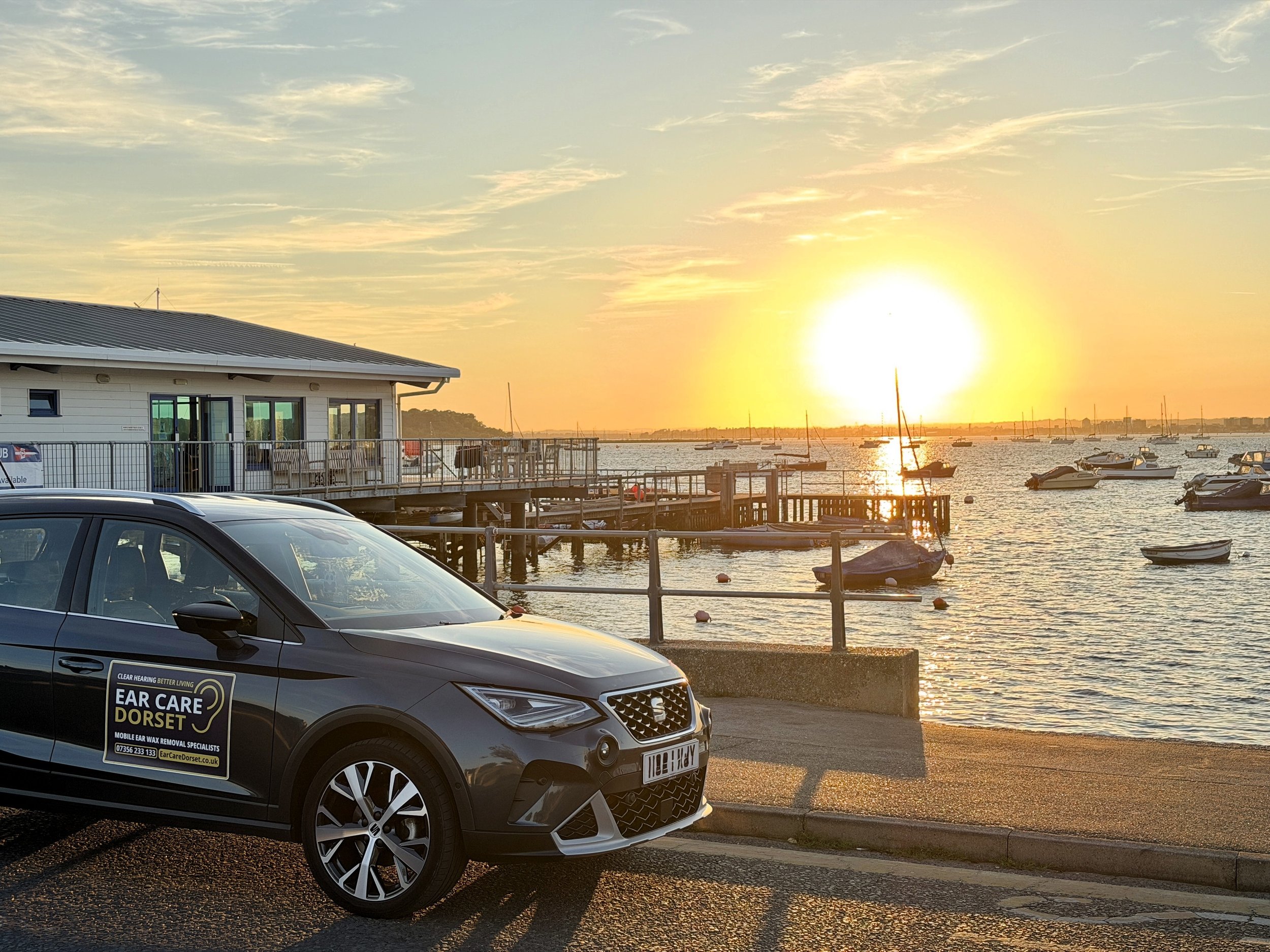 Ear Care Dorset branded car parked beside Sandbanks beach in Poole at sunset.