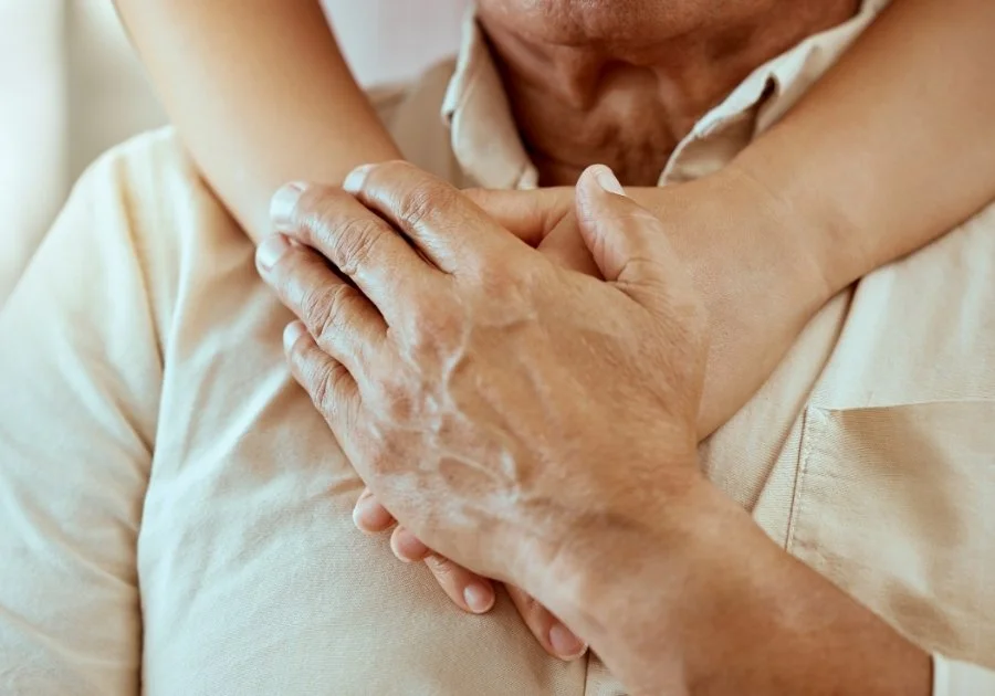 Close-up of an elderly man gently holding a young girl's arm across his chest, demonstrating comfort or affection.