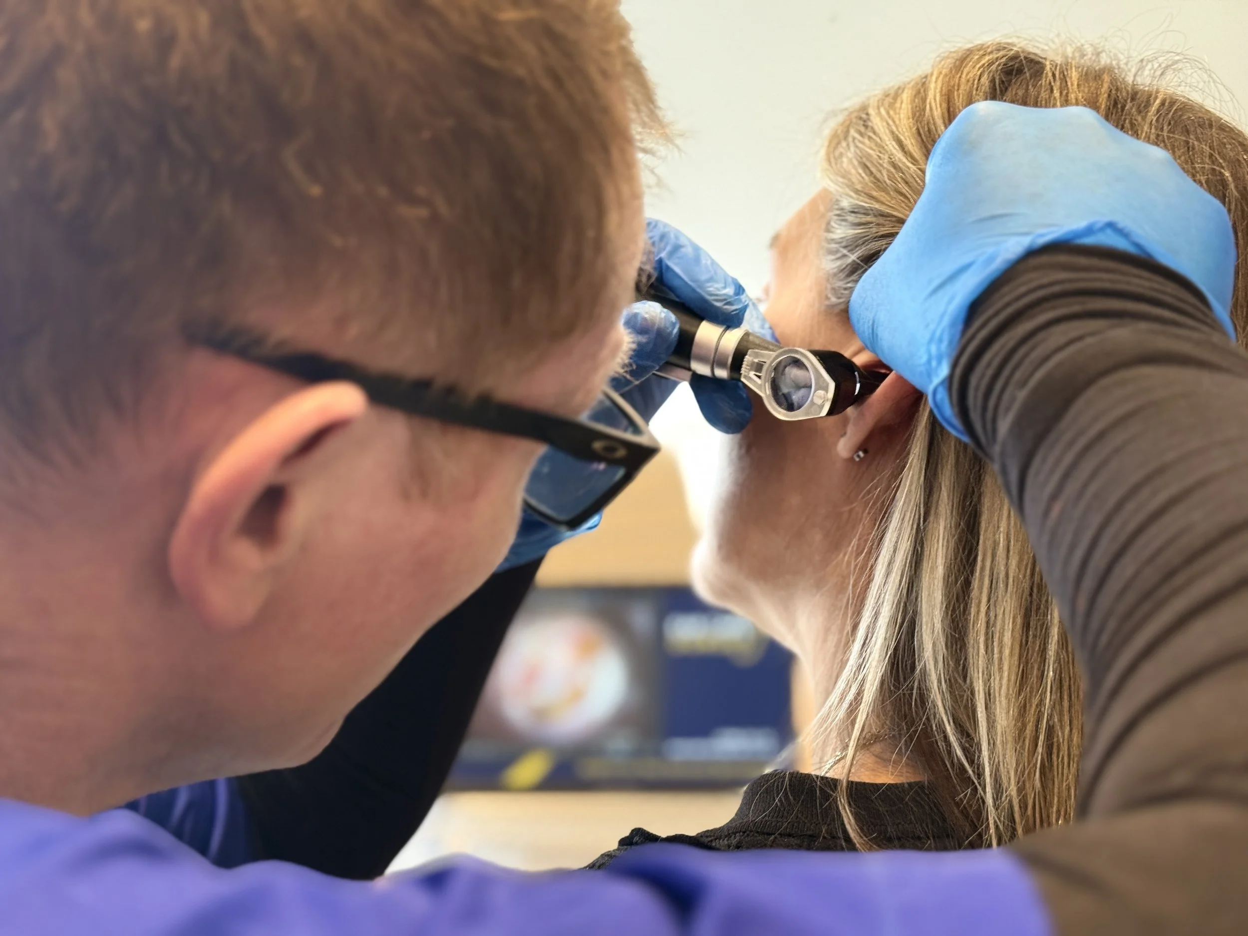 A close-up of our practitioner, Ryan, conducting a full ear health examination on a female patient with long hair using a otoscope.