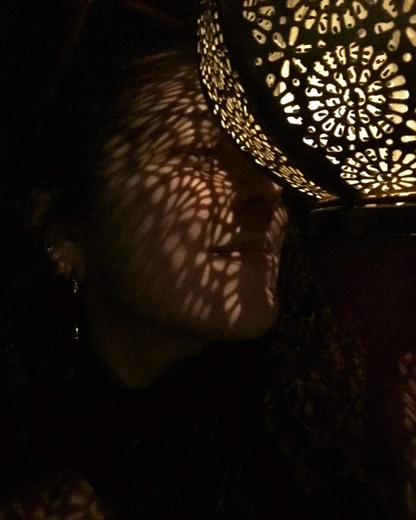 A decorative metallic lamp with intricate cut-out patterns casting shadows on surrounding surfaces in low light.