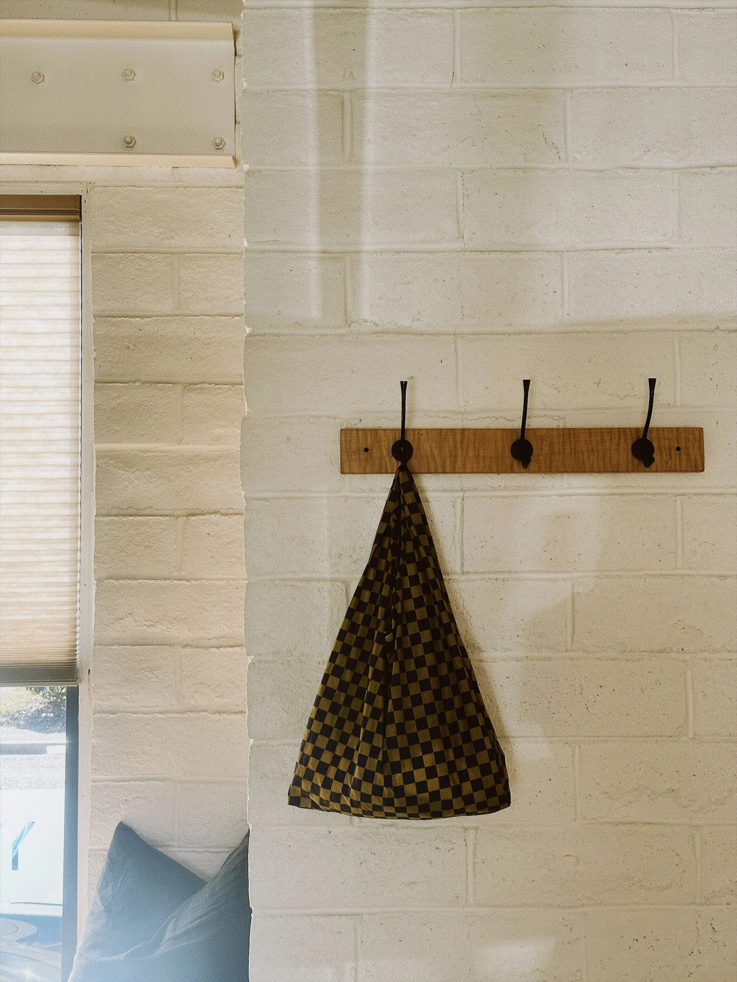 A wall with a wooden coat rack holding a checkered black and yellow cloth, adjacent to a window with blinds.