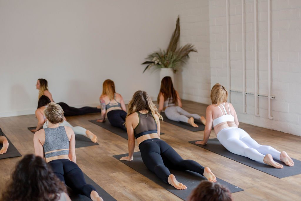 Group of women participating in a yoga class in a bright studio, practicing poses on mats.