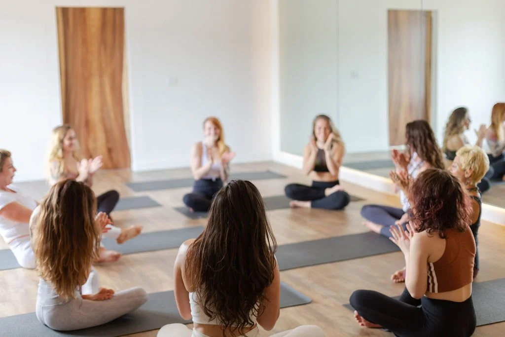 Group of women participating in a yoga or meditation class in a studio with wooden flooring and mirrors
