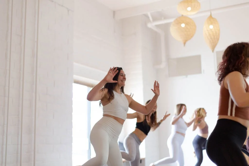 Women participating in a fitness class in a bright studio, performing aerobic exercises.