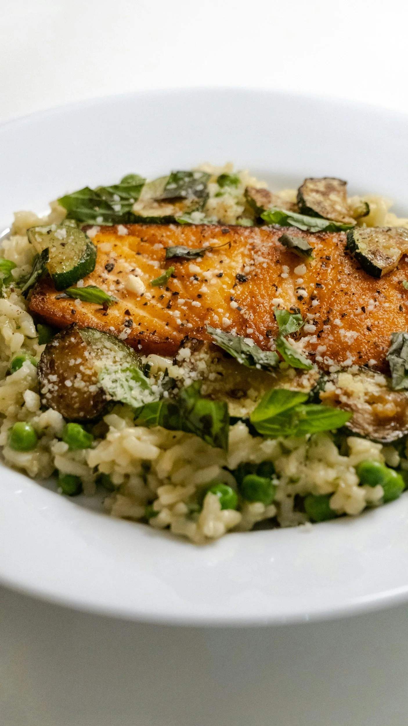 Close-up of a plated dish with grilled salmon, rice with peas, and sautéed zucchini and mushrooms, garnished with fresh herbs.
