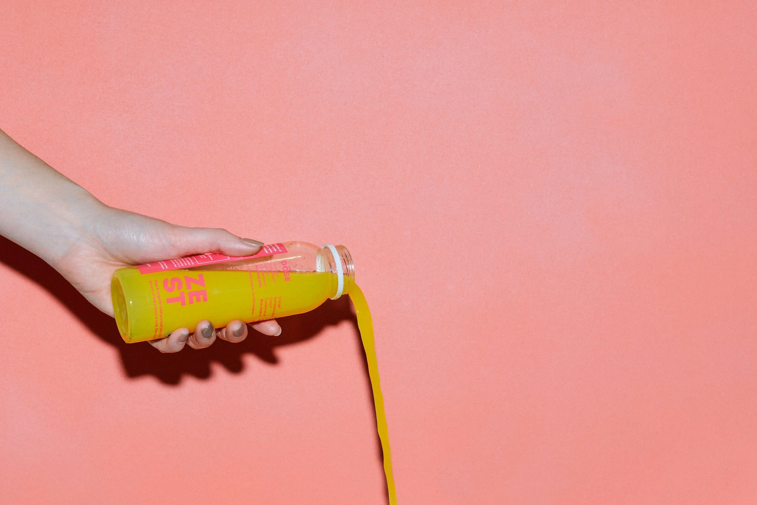 A hand holding a bright yellow drink called 'PEE ZEE' with a pink label and a yellow straw against a pink background.