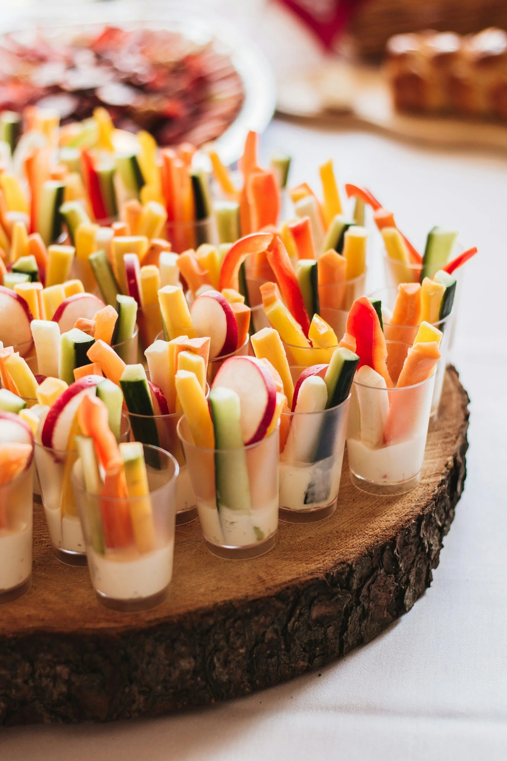 Assorted vegetable and cheese appetizers served in small clear cups on a rustic wooden serving board.