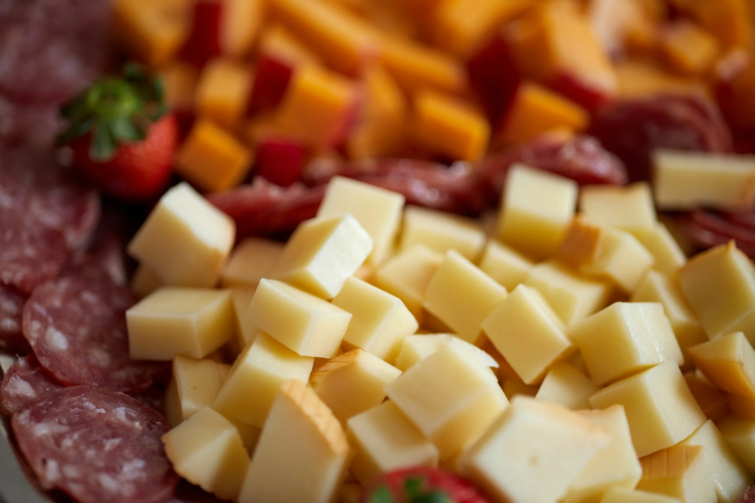 Close-up of a cheese and meat platter with cubed cheese, sliced cured meats, and strawberries on a serving dish.