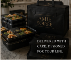 Black bag with gold lettering that says 'AMIE SOIRÉ,' three black food containers with salads and main dishes, and a sign that reads 'DELIVERED WITH CARE. DESIGNED FOR YOUR LIFE.'