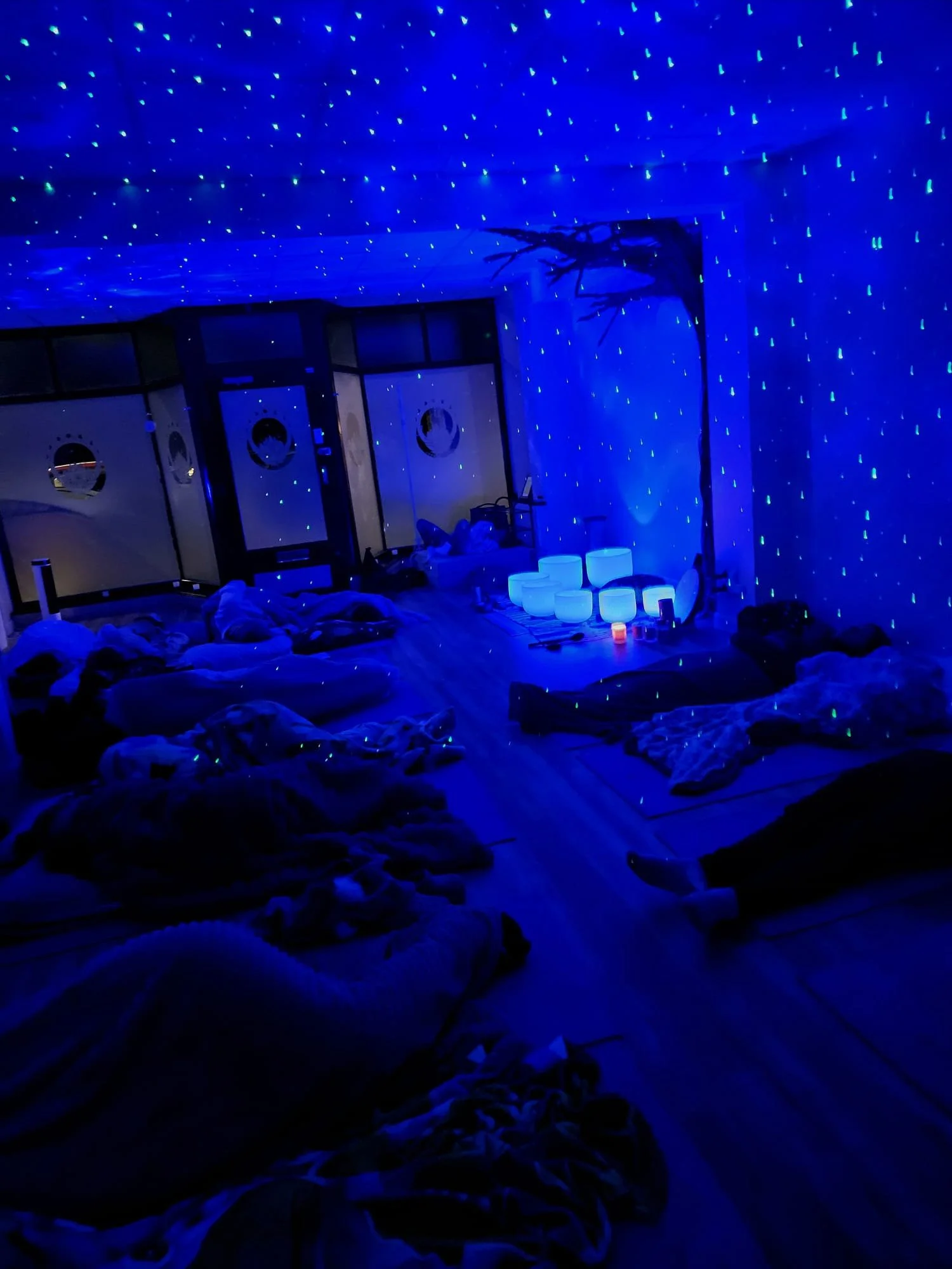 Room illuminated with blue LED star ceiling lights, with blankets and pillows scattered on the bed, and glow-in-the-dark or illuminated objects on the floor and table.
