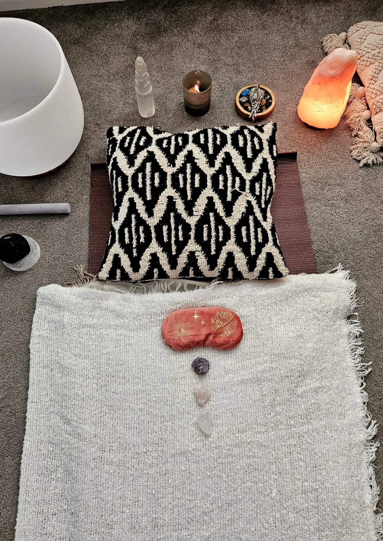 A spiritual or healing setup on a carpeted floor with various objects including gemstones, candles, salt lamp, and a patterned cushion, indicating a space for meditation or energy work.