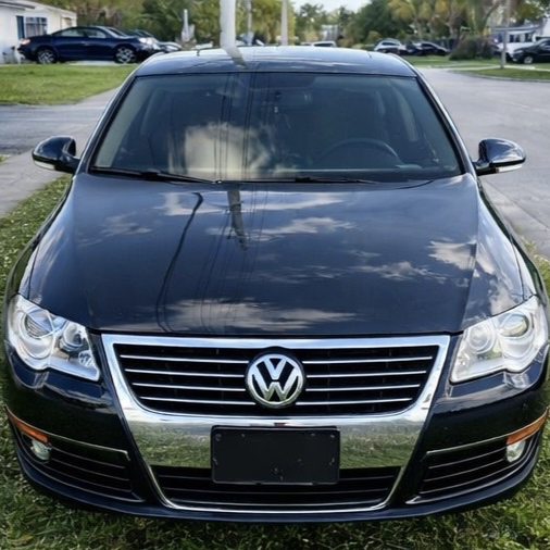 Front view of a black Volkswagen sedan parked on grass with other cars and trees in the background.