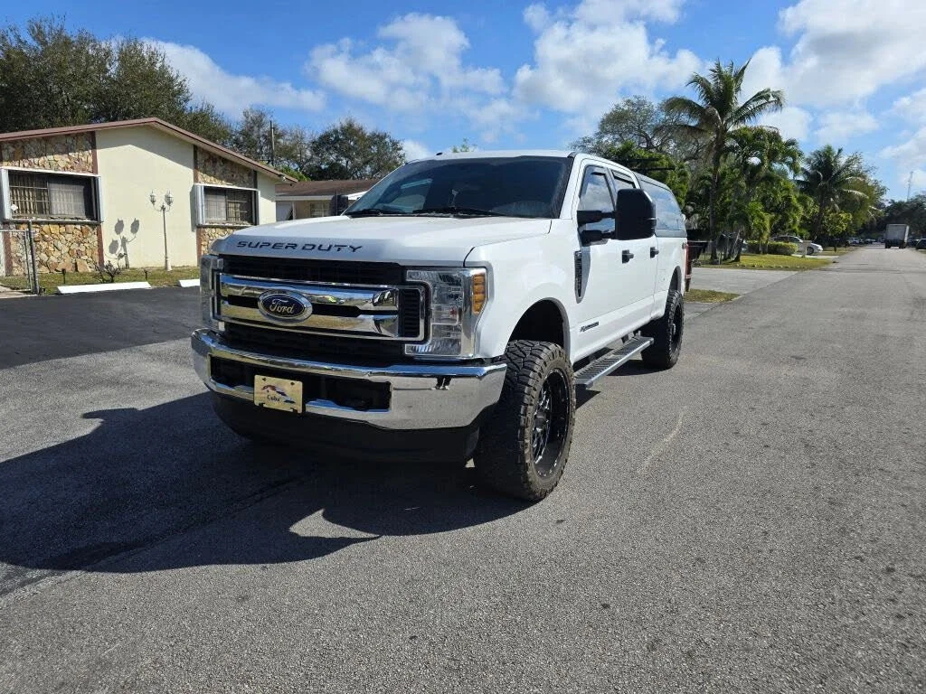 White Ford Super Duty pickup truck parked on a paved street in a suburban neighborhood with palm trees and houses.