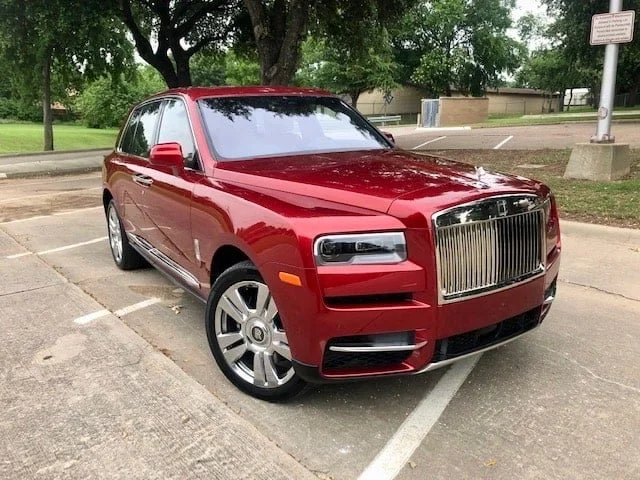 Red luxury SUV parked in a parking lot with trees and a sign in the background.