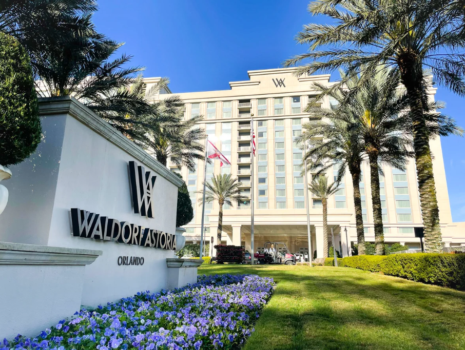 Exterior view of Waldorf Astoria Orlando hotel with lush landscaping, palm trees, and a sign in the foreground.