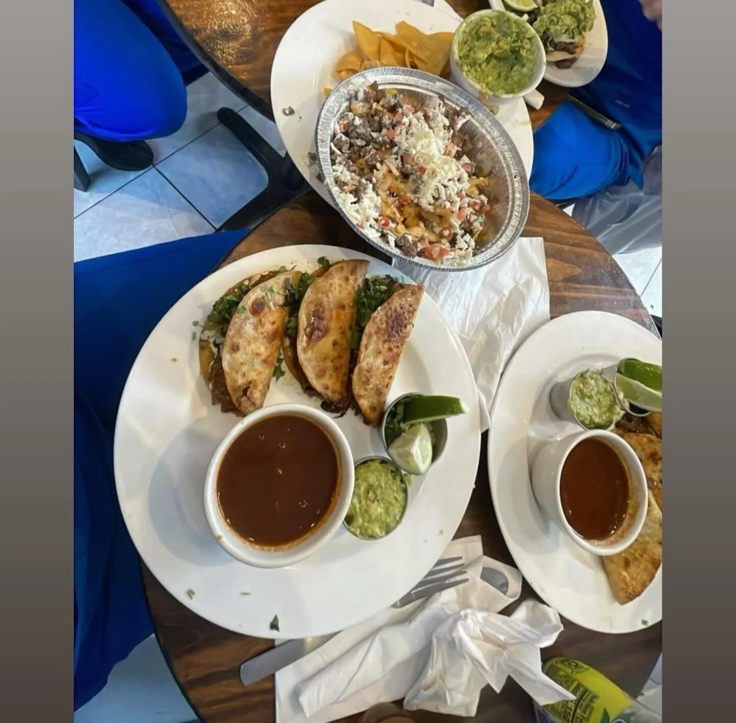 Table with Mexican dishes including tacos dorados, bowl of rice, guacamole, salsa, and drinks.