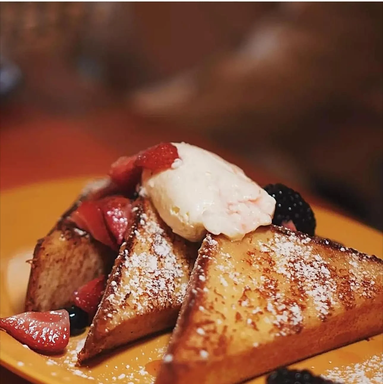 French toast topped with berries and whipped cream, dusted with powdered sugar.
