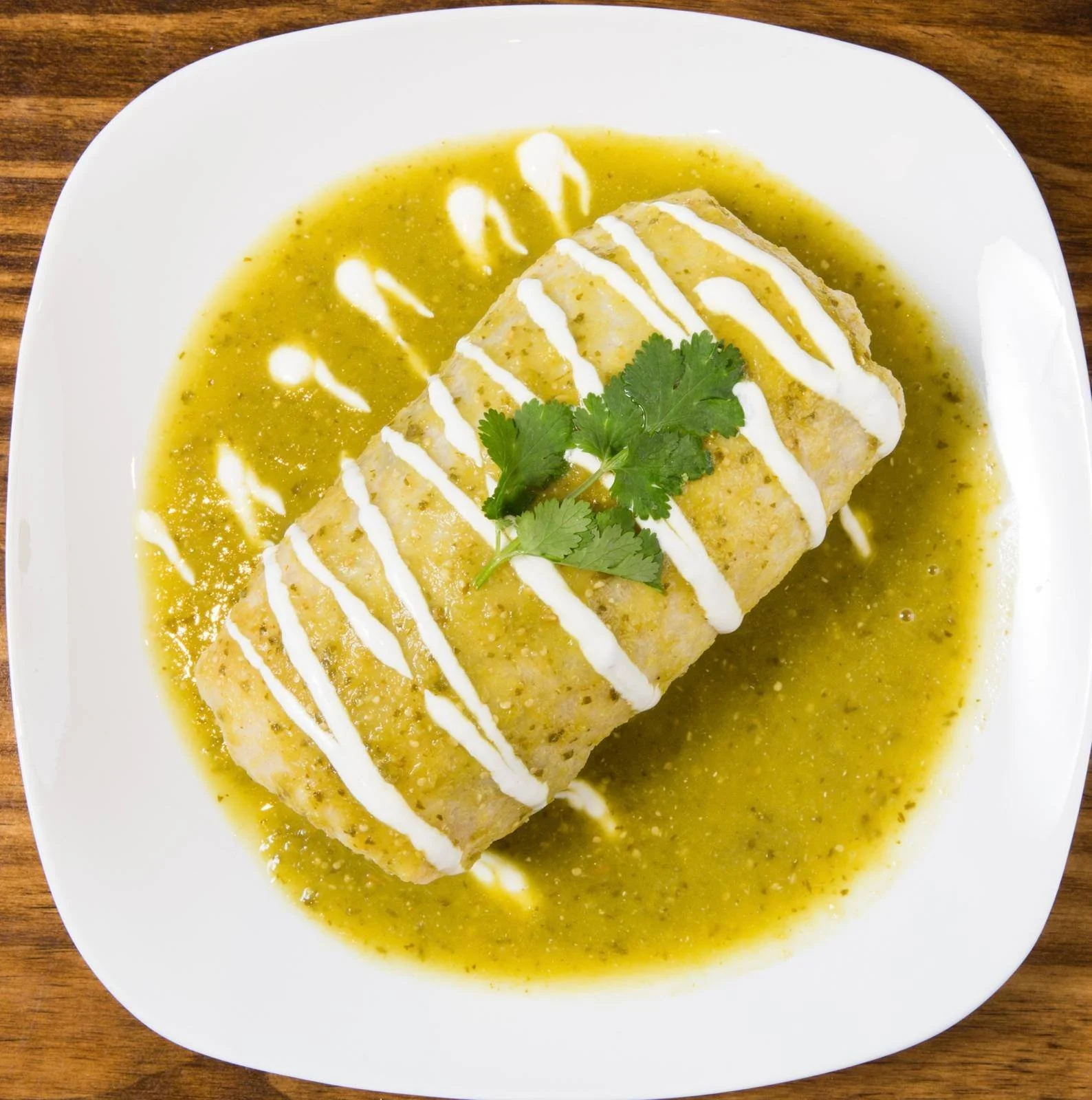 A plate with a fish taco covered in white sauce, topped with cilantro, served on a bed of green sauce with a drizzle of white sauce.