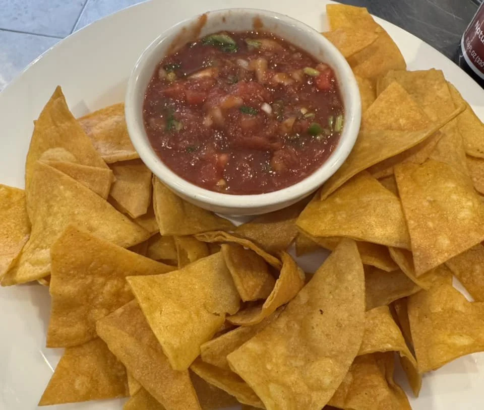 A plate of tortilla chips arranged around a bowl of salsa on a white plate.