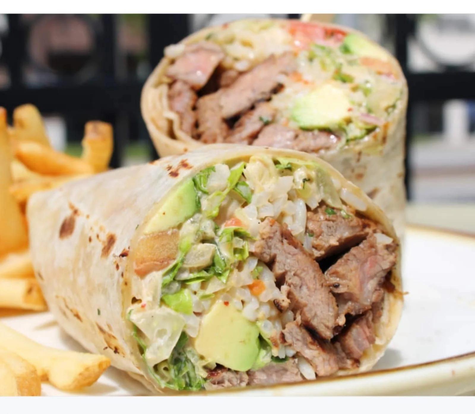 Close-up of a sliced beef and vegetable burrito with French fries on the side.