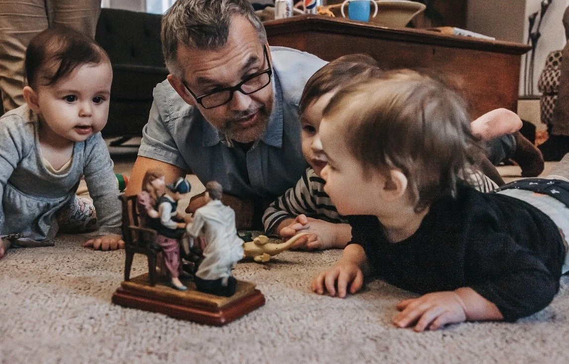 Author Denis Fortier  and three young children lying on the carpet, examining a small nativity figurine set.