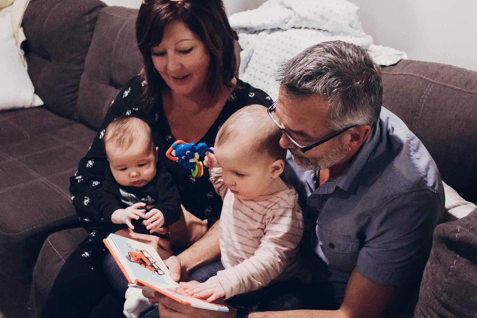 Author Denis Fortier, wife and two grandchildren sitting on a brown couch, looking at a children's book together.